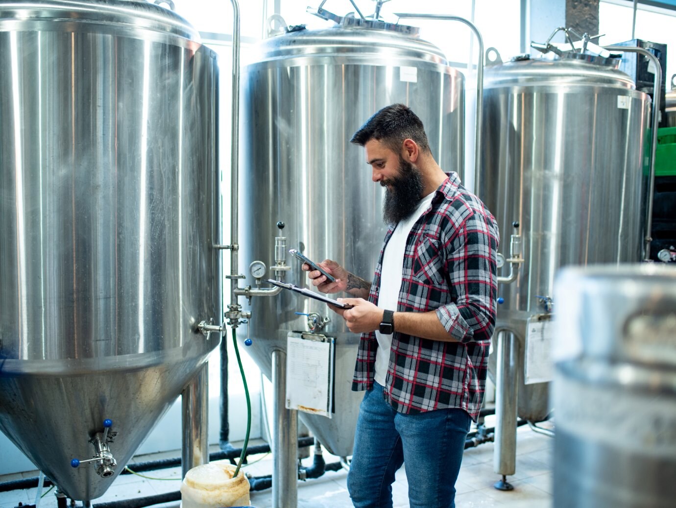 A person holding a mobile standing and monitoring the brewery processing unit